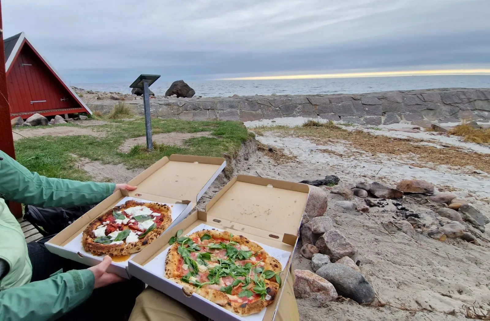 To pizzaer i åbne æsker på stranden ved Sandvig med Østersøen i baggrunden