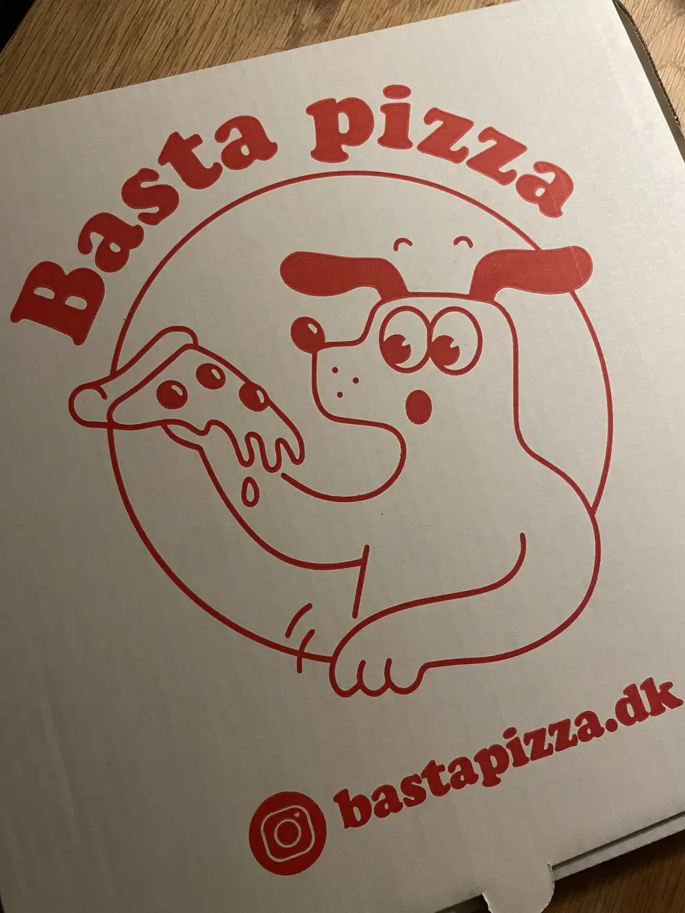 Basta Pizza-æske med hundemaskotten, der spiser et stykke pizza