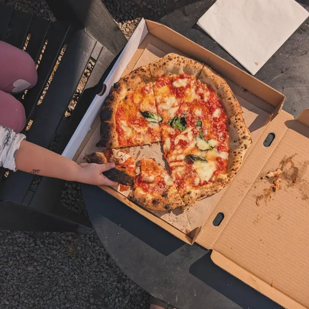 Frisk margherita-pizza i æske, holdt i én hånd