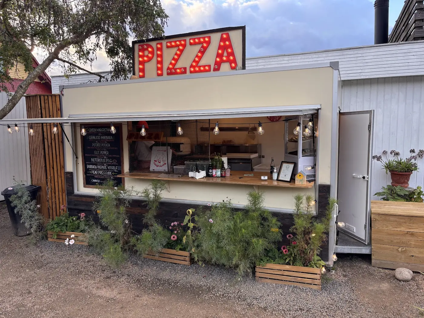 Basta Pizza-vognen med rødt PIZZA-lysskilt og blomsterkasser